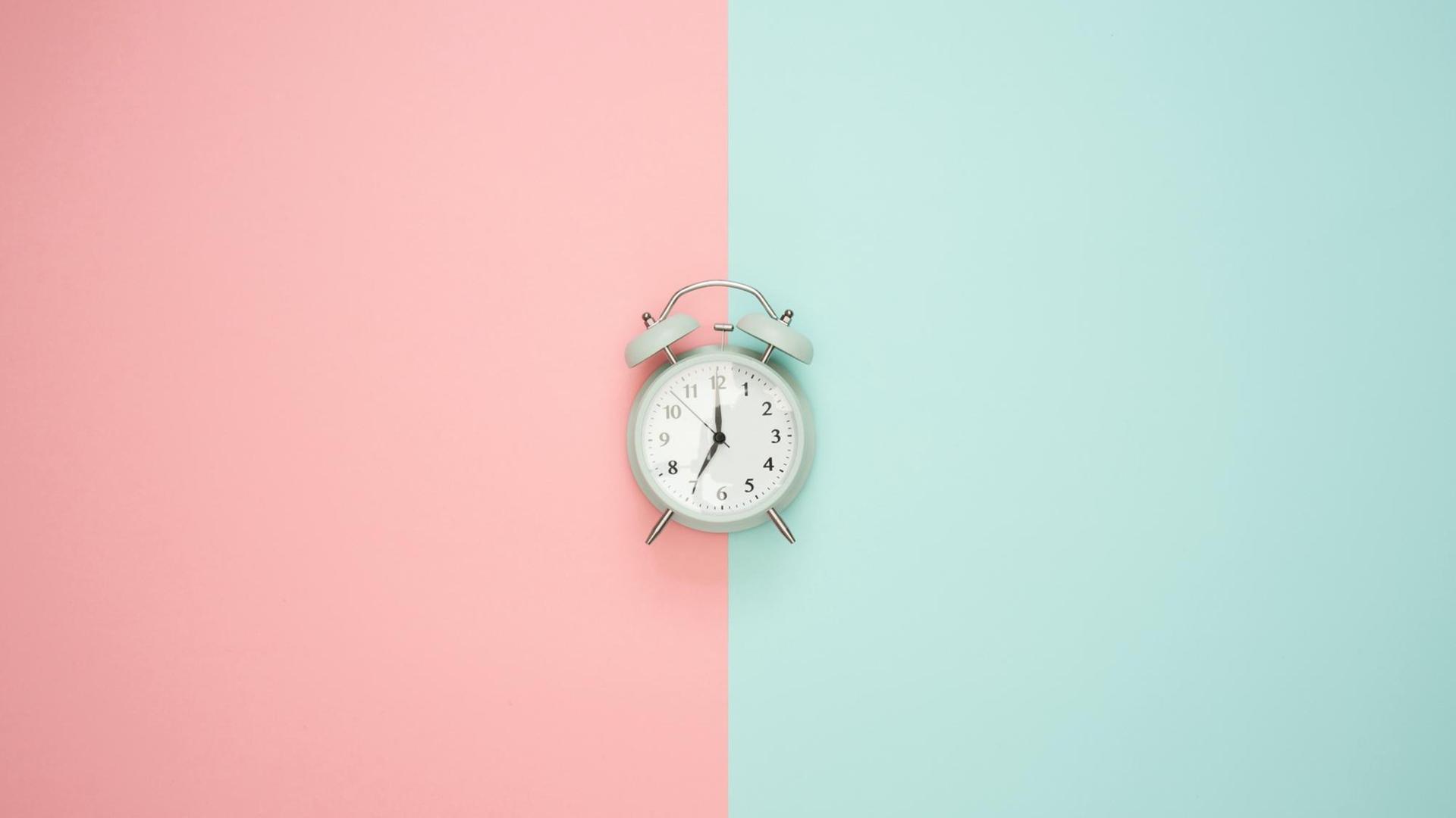 Ein Wecker auf buntem Hintergrund zeigt 19 Uhr an. Ein Wecker auf buntem Hintergrund zeigt 19 Uhr an.
