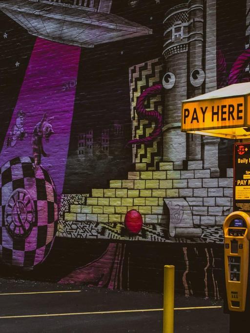 Ein Parkautomat vor einer Wand voller Graffitis.