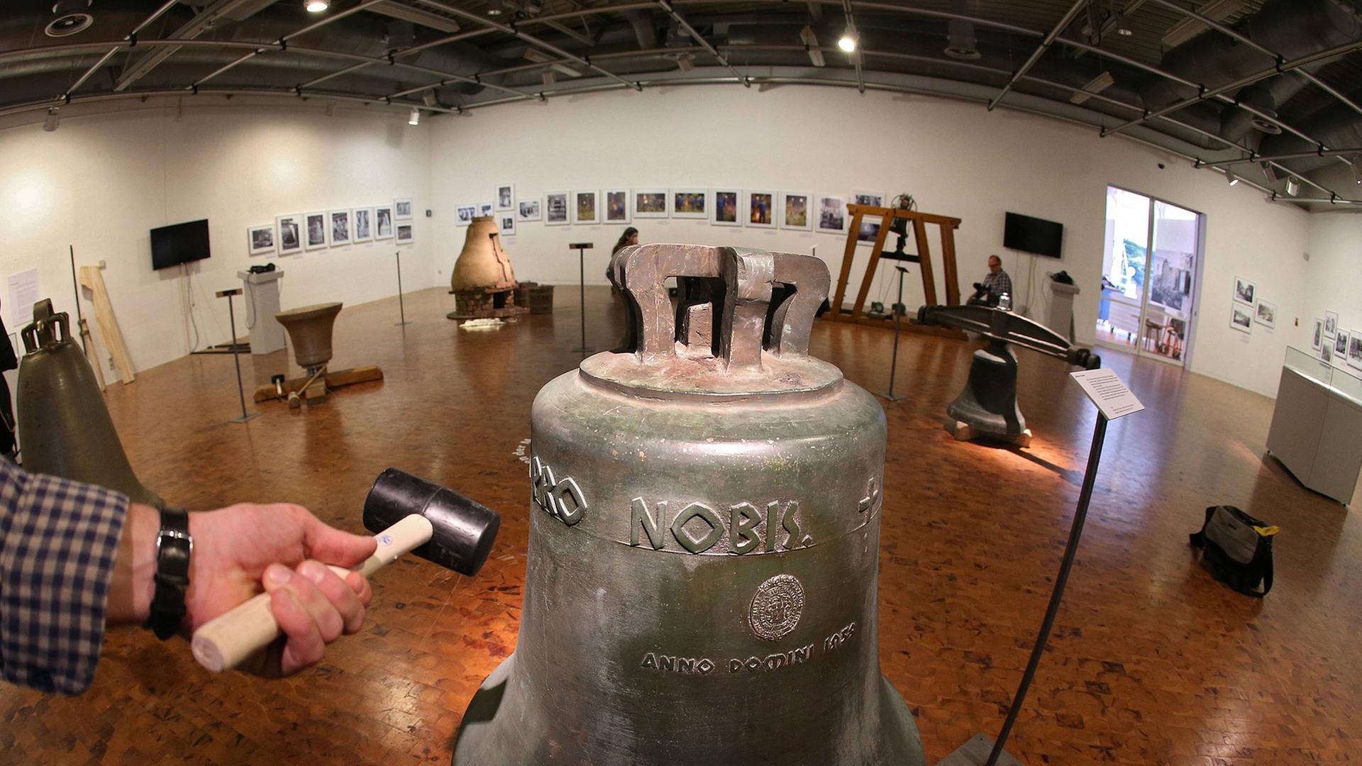 Hammer neben einer Glocke in einem Ausstellungsraum. Eine Ausstellung in Dortmund gibt Einblicke in das Glockenhandwerk. Hammer neben einer Glocke in einem Ausstellungsraum. Eine Ausstellung in Dortmund gibt Einblicke in das Glockenhandwerk.