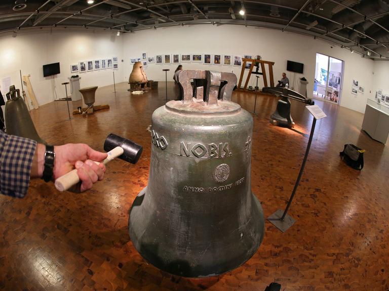 Hammer neben einer Glocke in einem Ausstellungsraum. Eine Ausstellung in Dortmund gibt Einblicke in das Glockenhandwerk.