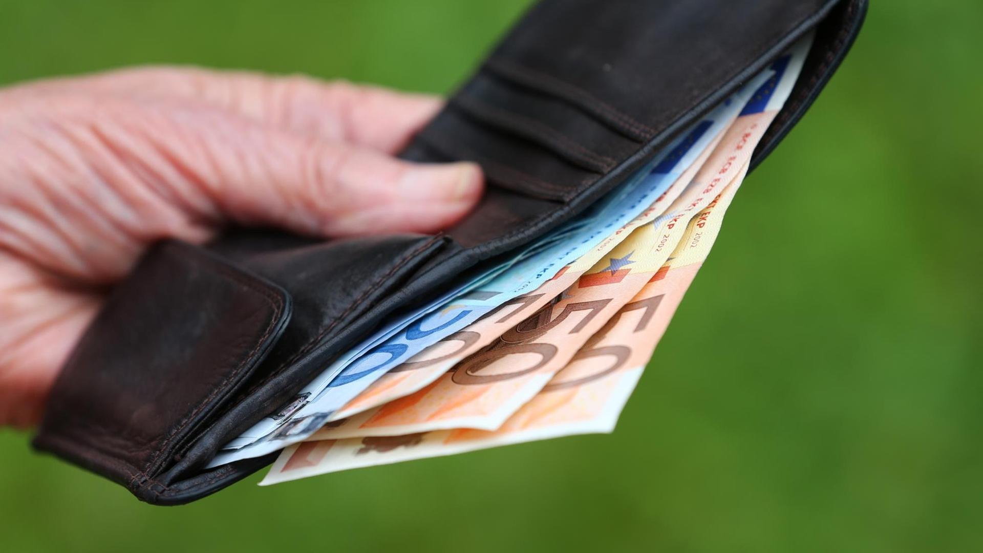 Eine faltige Hand hält eine Geldbörse, aus der Scheine ragen. Eine faltige Hand hält eine Geldbörse, aus der Scheine ragen.