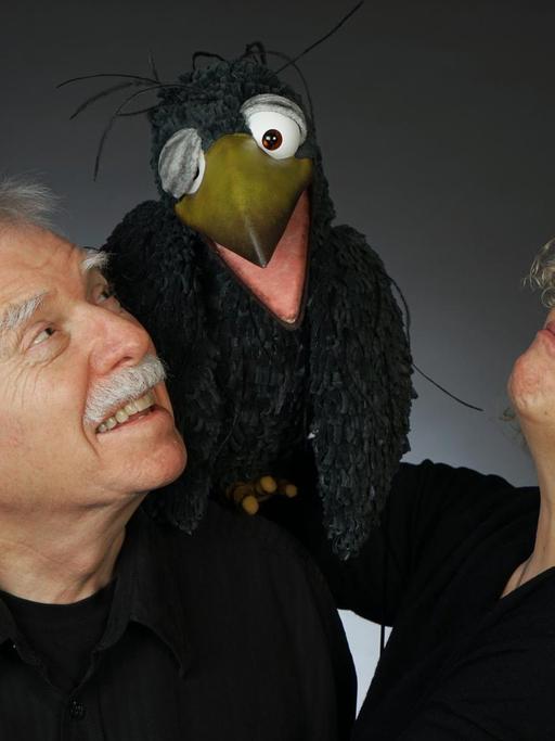 Claudia Röders trägt auf der Hand die Puppe Rudi, einen Raben, und setzt ihn fröhlich auf die Schulter ihres Mannes Peter Röders.