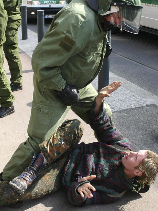 Ein Polizist steht drohend über einem Punk, der am Boden liegt.