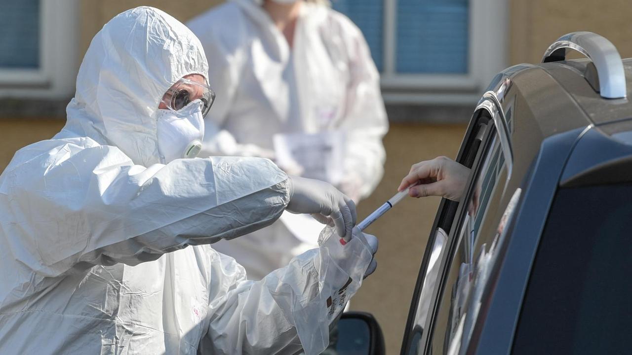 Ein Arzt in Schutzausrüstung nimmt an einem Corona-Testzentrum auf dem Gelände einer Berufsschule den Abstrichtest auf das Coronavirus Sars-Cov-2 von einem Autofahrer entgegen.