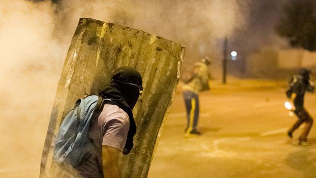 In der venezuelanischen Stadt Altamira ist am 24.02.2014 ein vermummter Demonstrant zu sehen, der einen Schild aus Wellblech trägt und von Qualm umgeben ist.