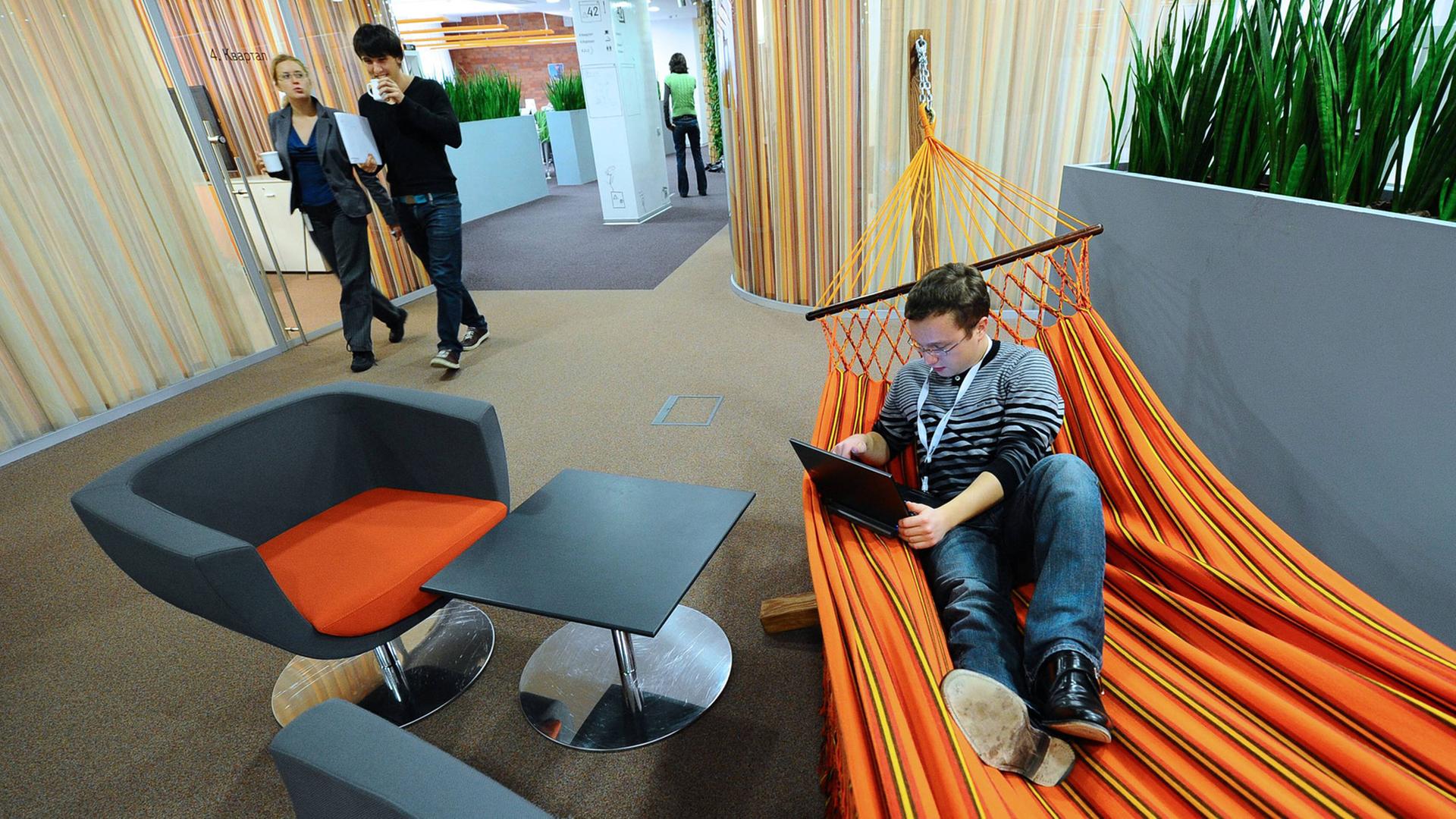 Ein Mitarbeiter im Moskauer Büro des Internetdienstleisters Yandex liegt mit Laptop in einer orangefarbenen Hängematte. Ein Mitarbeiter im Moskauer Büro des Internetdienstleisters Yandex liegt mit Laptop in einer orangefarbenen Hängematte.