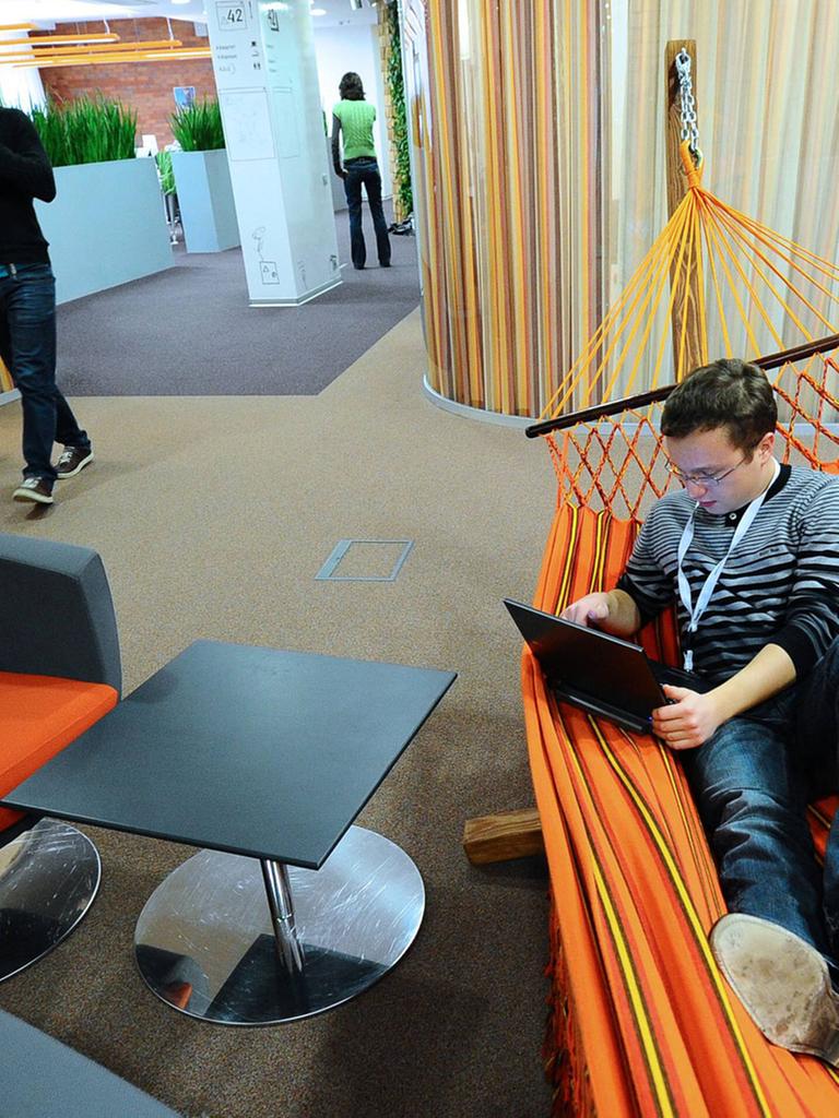Ein Mitarbeiter im Moskauer Büro des Internetdienstleisters Yandex liegt mit Laptop in einer orangefarbenen Hängematte.