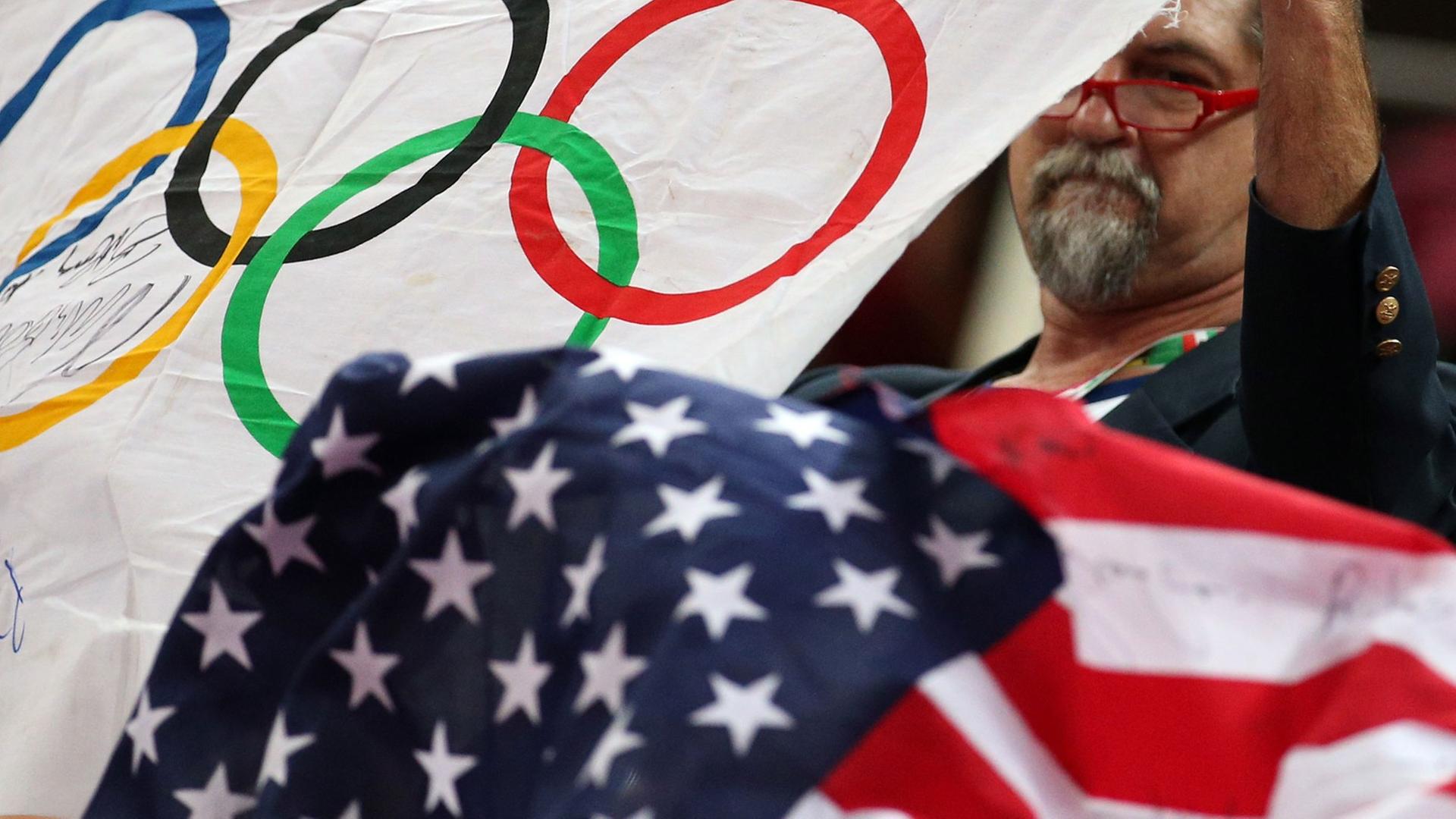 Ein Mann hält die Olympische Flagge und die der USA in die Höhe. Ein Mann hält die Olympische Flagge und die der USA in die Höhe.
