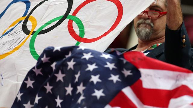 Ein Mann hält die Olympische Flagge und die der USA in die Höhe.