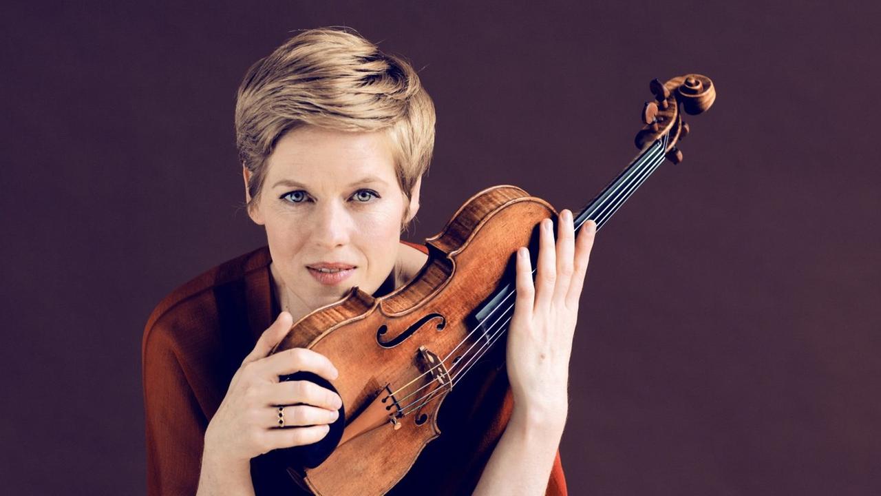 Die Geigerin mit kurzem Haar hält ihr Instrument halb schräg an ihr Kinn. Die Geigerin mit kurzem Haar hält ihr Instrument halb schräg an ihr Kinn.