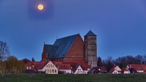 Ein großer Mond erscheint über der Stadt Verden mit seinem Dom und den umgebenden Wiesen.