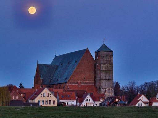 Ein großer Mond erscheint über der Stadt Verden mit seinem Dom und den umgebenden Wiesen.