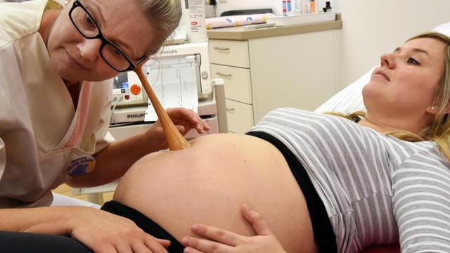 Hebamme Simone Scherer überprüft mit einem Holzstethoskop als Alternative zur Kardiotokographie die Herztöne des ungeborenen Kindes bei der Medizinstudentin Nadja Schwark.