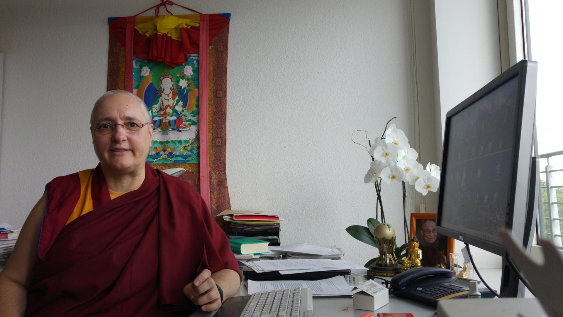 Die tibetisch-buddhistische Nonne Carola Roloff sitzt an einem Schreibtisch und blickt in die Kamera. Die tibetisch-buddhistische Nonne Carola Roloff sitzt an einem Schreibtisch und blickt in die Kamera.