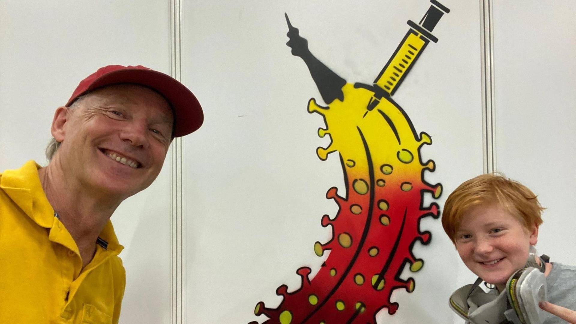 Ein Mann im gelben Shirt lacht links in die Kamera, ein Junge rechts. Dazwischen ist ein Bild einer Banane zu sehen, die oben gelb ist und unten rot ist und dort auch Noppen an der Schale hat. Oben steckt in der Banane eine gelbe Spritze. Ein Mann im gelben Shirt lacht links in die Kamera, ein Junge rechts. Dazwischen ist ein Bild einer Banane zu sehen, die oben gelb ist und unten rot ist und dort auch Noppen an der Schale hat. Oben steckt in der Banane eine gelbe Spritze.