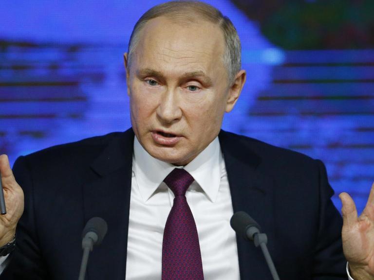 Der russische Präsident Putin steht auf seiner jährlichen Pressekonferenz vor Mikrofonen und hebt beide Hände.