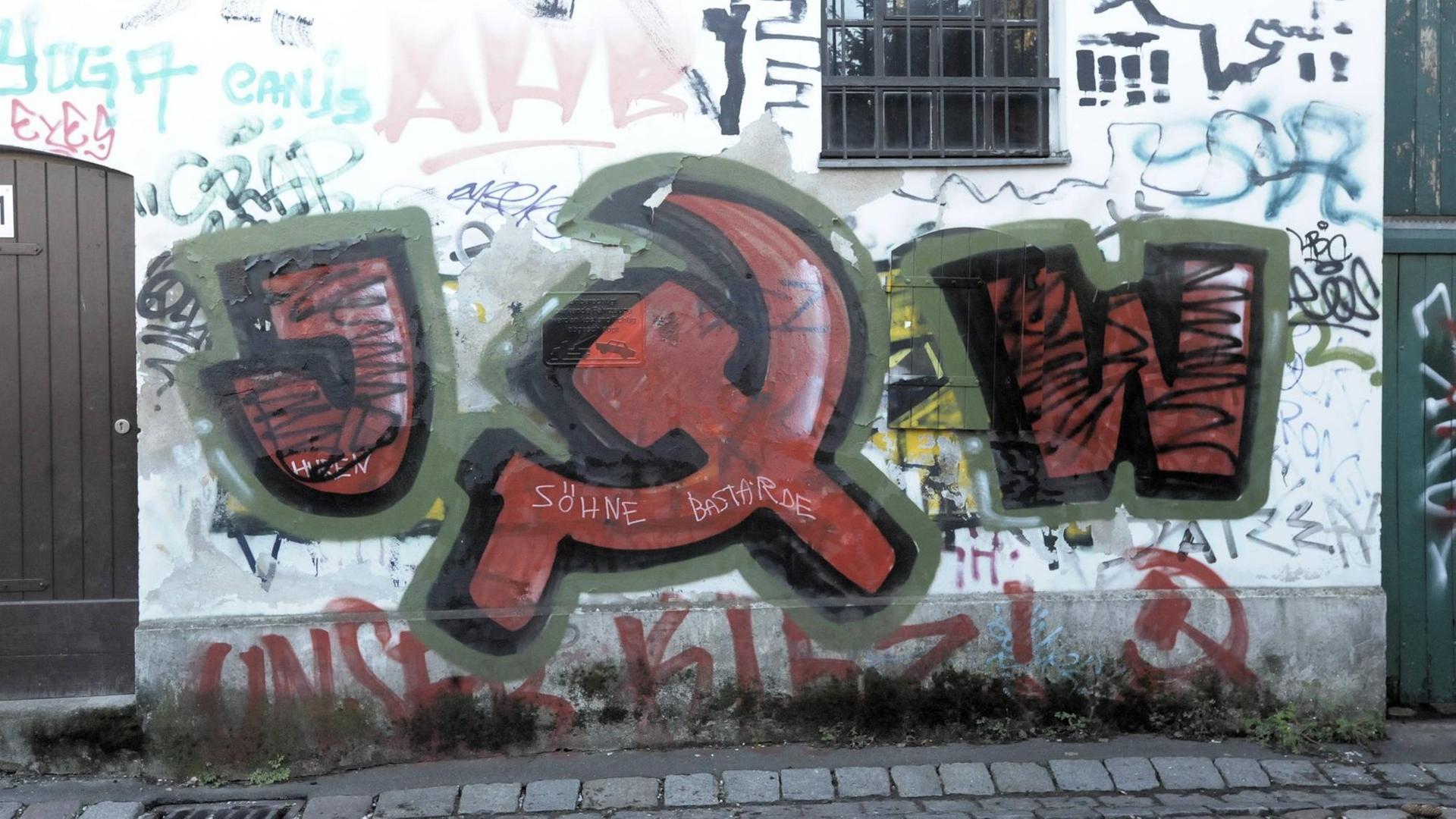 Auf einer Hauswand in der Neuköllner Kirchgasse im Böhmischen Dorf hat jemand ein Graffiti angebracht mit dem Kürzel JW für Jugendwiderstand und dem Symbol Hammer und Sichel.
