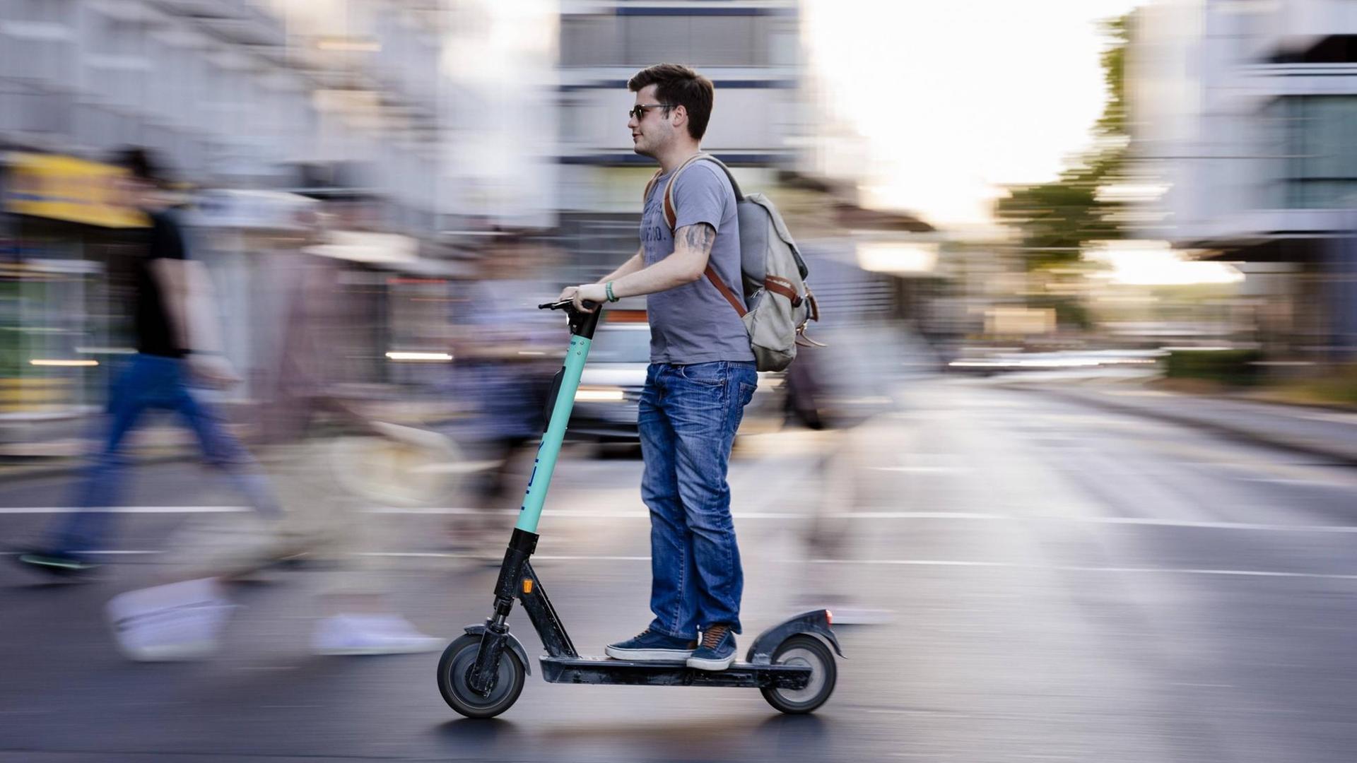 Ein Mann auf einem E-Scooter fährt über die Straße. Ein Mann auf einem E-Scooter fährt über die Straße.