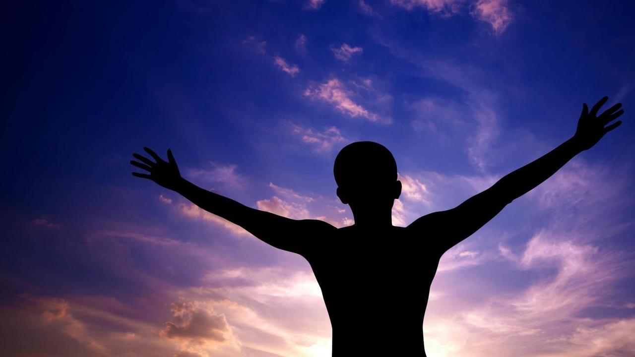 Mann breitet seine Arme aus. Seine Silhouette hebt sich gegen einen farbigen Himmel ab. Mann breitet seine Arme aus. Seine Silhouette hebt sich gegen einen farbigen Himmel ab.