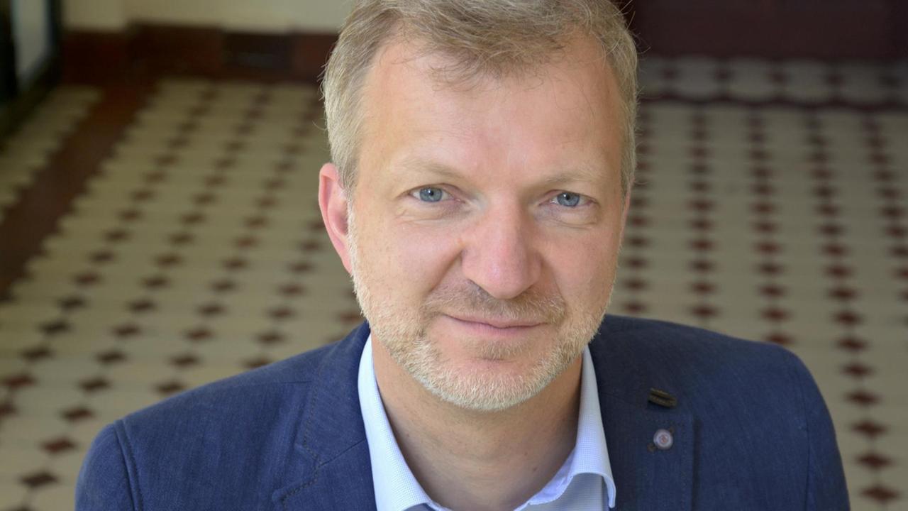 Thomas Großbölting im blauen Jacket blickt leicht von unten freundlich in die Kamera. Thomas Großbölting im blauen Jacket blickt leicht von unten freundlich in die Kamera.