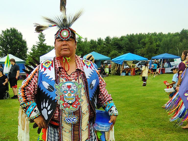 Ein Gast auf dem Pow Wow in Ontario, im Hintergrund tanzende Mädchen.