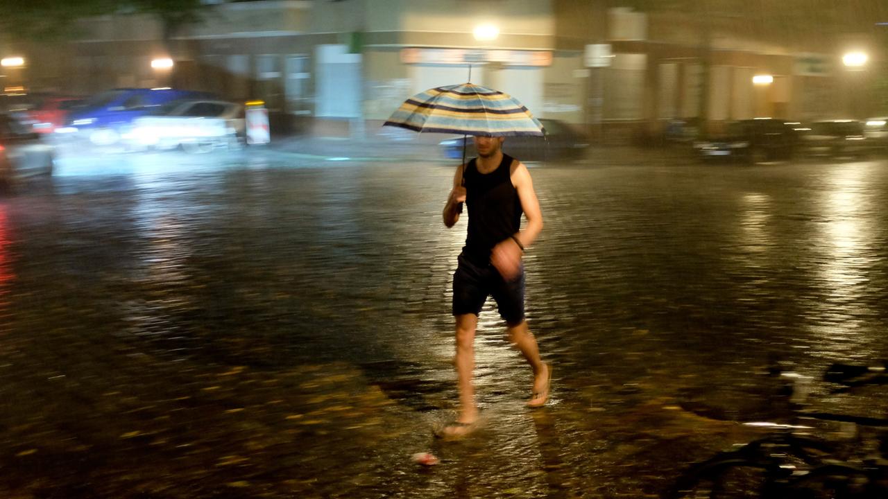 Ein Passant läuft mit einem Regenschirm über eine Kreuzung.