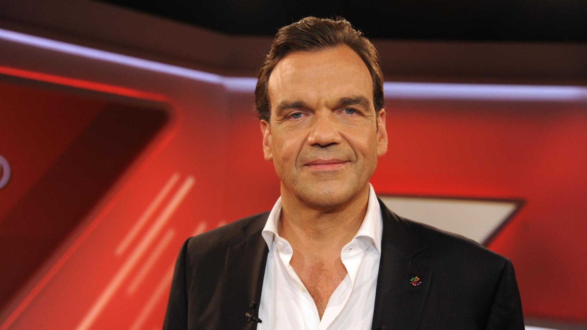 Christoph Gröner steht in einem rot gestalteten Studio und schaut freundlich in die Kamera Christoph Gröner steht in einem rot gestalteten Studio und schaut freundlich in die Kamera
