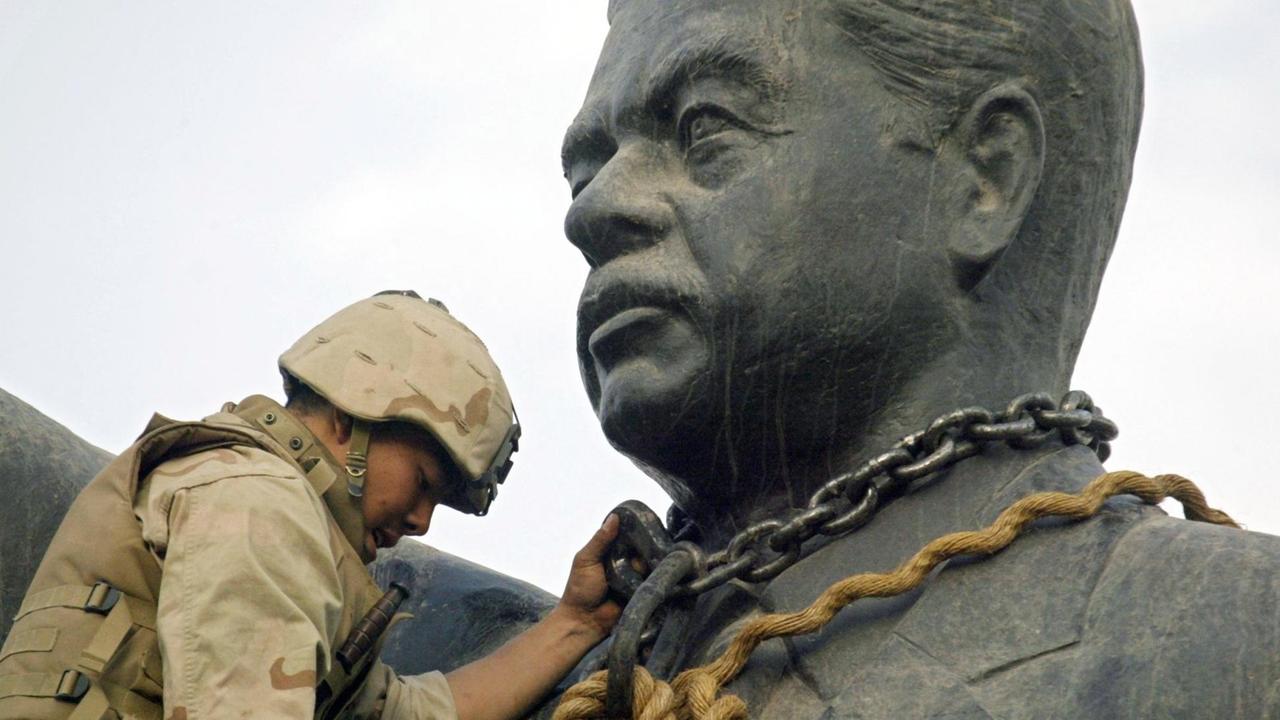 Ein US-Soldat legt eine Kette um den Kopf der Statue von Saddam Hussein, was auch symbolische den Sturz des Diktators verbildlicht.