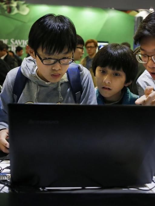 Vier Kinder in China drängen sich vor einen Computerbildschirm.