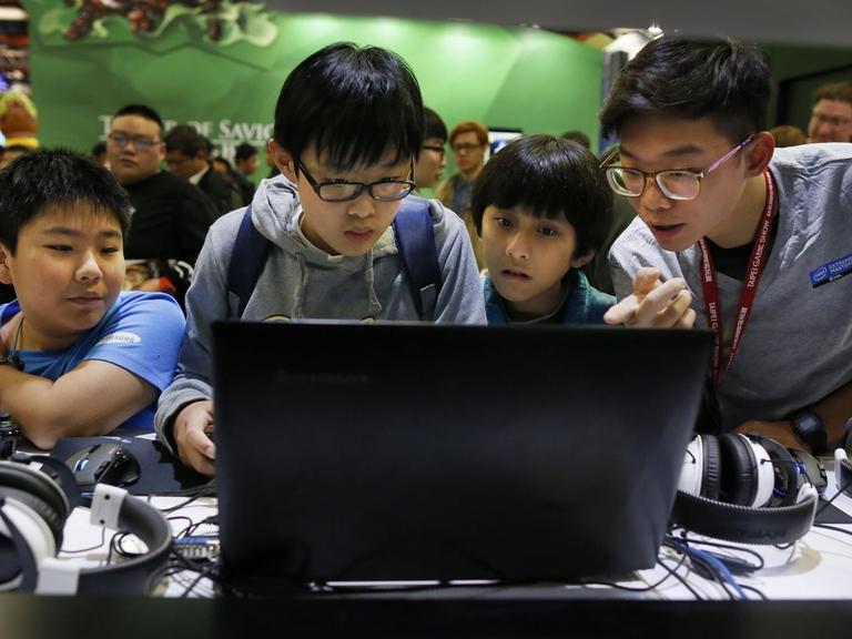 Vier Kinder in China drängen sich vor einen Computerbildschirm.