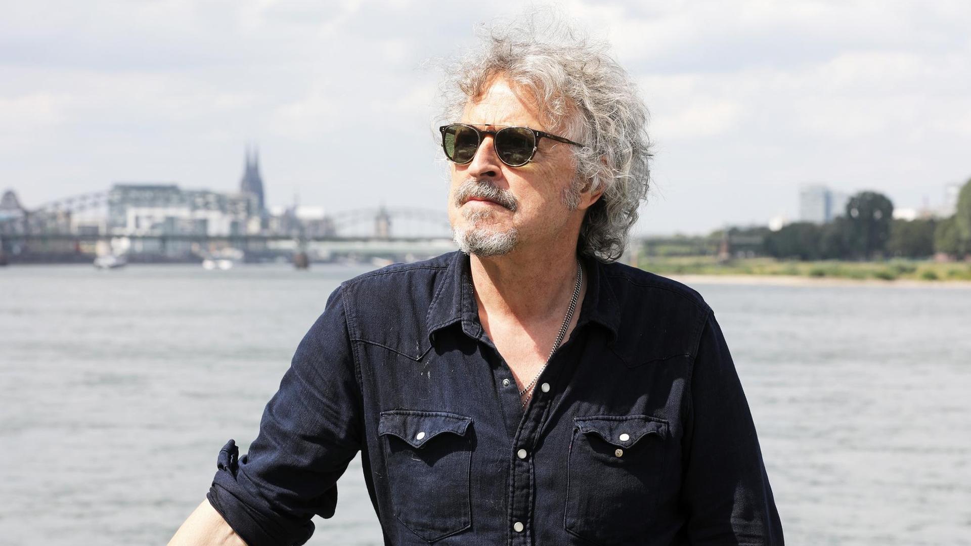 Der Musiker und Sänger Wolfgang Niedecken steht mit Sonnerbrille am Rheinufer. Der Musiker und Sänger Wolfgang Niedecken steht mit Sonnerbrille am Rheinufer.