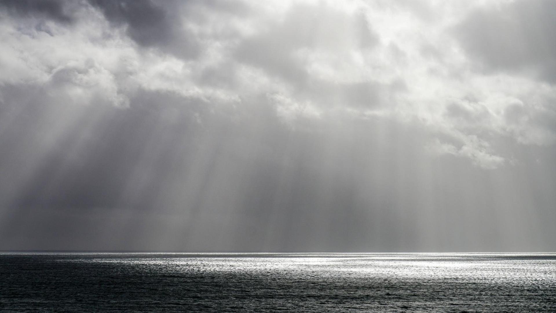 Sonnenstrahlen durchbrechen die Wolken ueber dem Atlantik vor der portugiesischen Küste