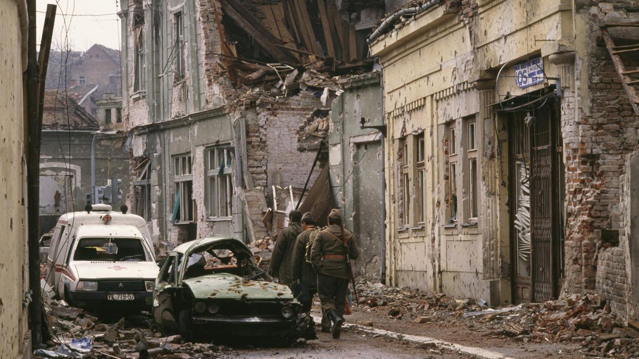 Jugoslawische Soldaten und serbische Paramilitärs, darunter Zeljko "Arkan" Raznatovic, ziehen nach einem dreimonatigen Kampf zwischen den kroatischen Streitkräften und der jugoslawischen Bundesarmee durch Vukovar an bombardierten, von Einschusslöchern durchlöcherten Gebäuden und mit Trümmern gefüllten Straßen vorbei. Die jugoslawische Bundesarmee zerstörte die kroatische Stadt vollständig und tötete Tausende von Zivilisten. Jugoslawische Soldaten und serbische Paramilitärs, darunter Zeljko "Arkan" Raznatovic, ziehen nach einem dreimonatigen Kampf zwischen den kroatischen Streitkräften und der jugoslawischen Bundesarmee durch Vukovar an bombardierten, von Einschusslöchern durchlöcherten Gebäuden und mit Trümmern gefüllten Straßen vorbei. Die jugoslawische Bundesarmee zerstörte die kroatische Stadt vollständig und tötete Tausende von Zivilisten.