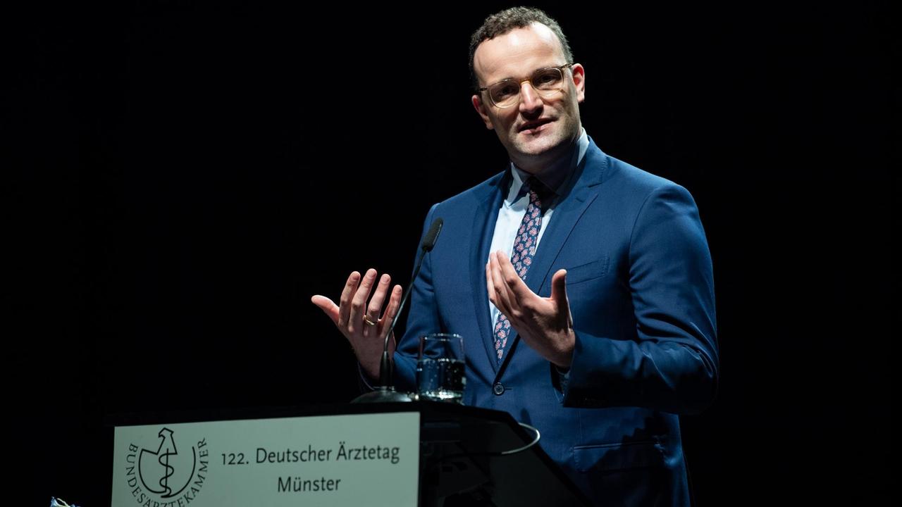 Spahn gestikuliert mit beiden Händen am Rednerpult, an dem das Schild "122. Deutscher Ärztetag" hängt. Der HIntergrund ist schwarz. Spahn gestikuliert mit beiden Händen am Rednerpult, an dem das Schild "122. Deutscher Ärztetag" hängt. Der HIntergrund ist schwarz.