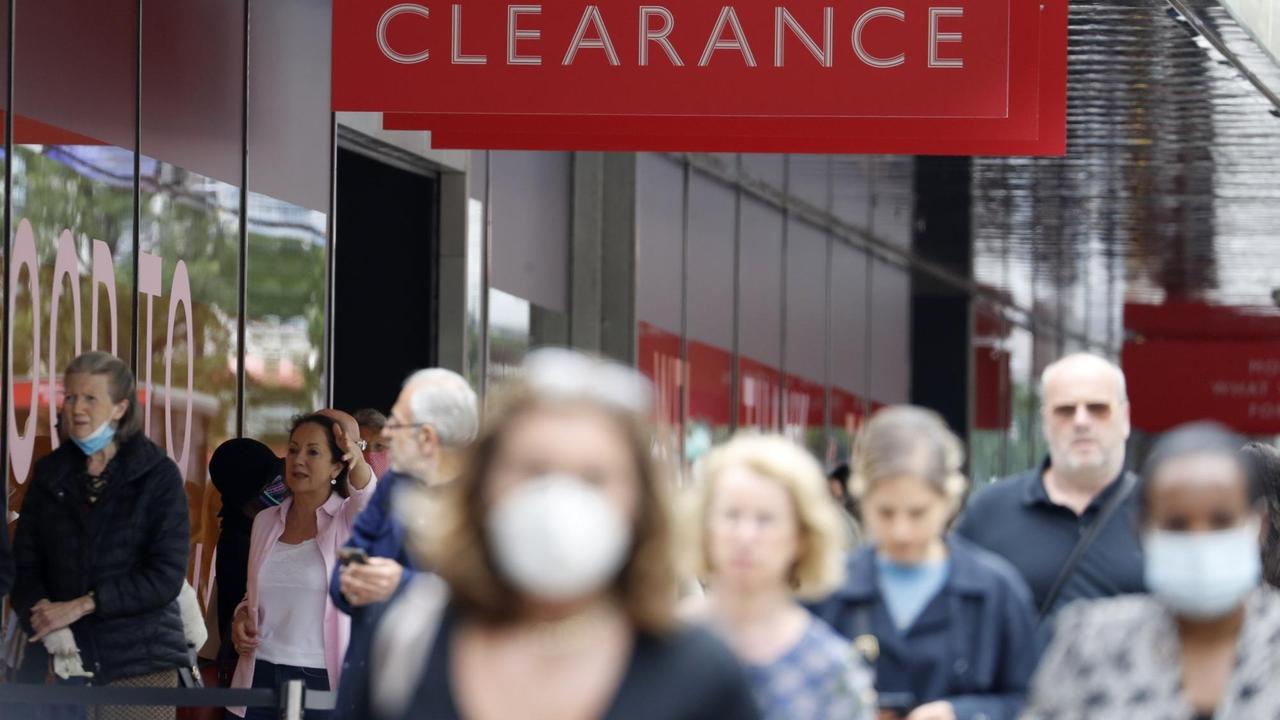 Eine Frau im Vordergrund ist nur unscharf zu sehen, die Menschen im Hintergrund teils scharf. Einige tragen Mund-Nasen-Masken. Über ihnen hängt ein rotes Schild mit der Aufschrift "Clearance", im Hintergrund eine Glasfront. Eine Frau im Vordergrund ist nur unscharf zu sehen, die Menschen im Hintergrund teils scharf. Einige tragen Mund-Nasen-Masken. Über ihnen hängt ein rotes Schild mit der Aufschrift "Clearance", im Hintergrund eine Glasfront.
