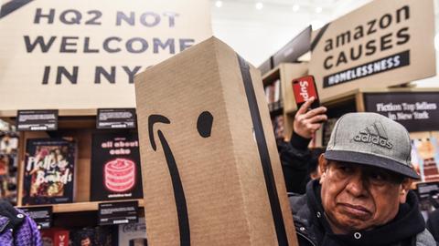 Ein Mann hält ein Paket in der Hand, auf dem das Amazon Logo anders herum abgedruckt ist, sodass sich ein trauriger Smiley ergibt.