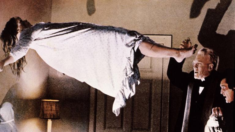 Szene aus dem Horrorfilm "Der Exorzist". Ein Mädchen im Nachthemd schwebt in einem Zimmer in der Luft, ein Priester macht beschwörende Gesten Szene aus dem Horrorfilm "Der Exorzist". Ein Mädchen im Nachthemd schwebt in einem Zimmer in der Luft, ein Priester macht beschwörende Gesten