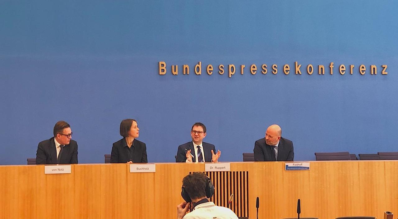 Vier Menschen mit Namensschildern hinter einem breiten Konferenztisch. Darüber die Aufschrift: "Bundespressekonferenz". Vier Menschen mit Namensschildern hinter einem breiten Konferenztisch. Darüber die Aufschrift: "Bundespressekonferenz".