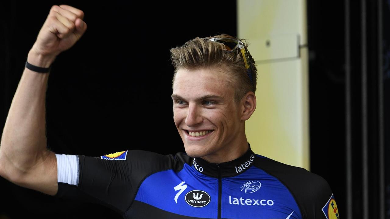 Kittel steht vor einer schwarzen Wand und hebt grinsend die geballte Faust. Kittel steht vor einer schwarzen Wand und hebt grinsend die geballte Faust.
