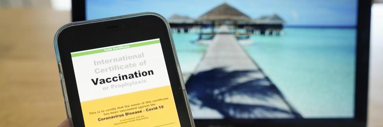 Symbolfoto: Digitaler Impfass und Reisepass vor Fernweh-Motiv auf einem Laptop. Symbolfoto: Digitaler Impfass und Reisepass vor Fernweh-Motiv auf einem Laptop.