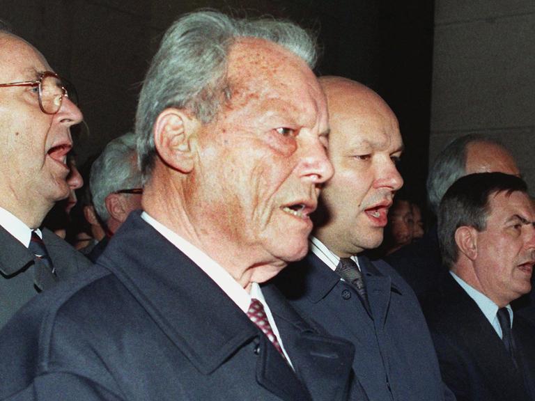 Bundesaußenminister Hans-Dietrich Genscher (FDP), Altbundeskanzler Willy Brandt (SPD), Berlins Regierender Bürgermeister Walter Momper (SPD), Jürgen Wohlrabe, Präsident des Berliner Abgeordnetenhauses, und Kanzleramtsminister Rudolf Seiters (CDU), singen bei der zentralen Kundgebung nach der Öffnung der Mauer am 10. November 1989 vor dem Schöneberger Rathaus in West-Berlin die Nationalhymne.