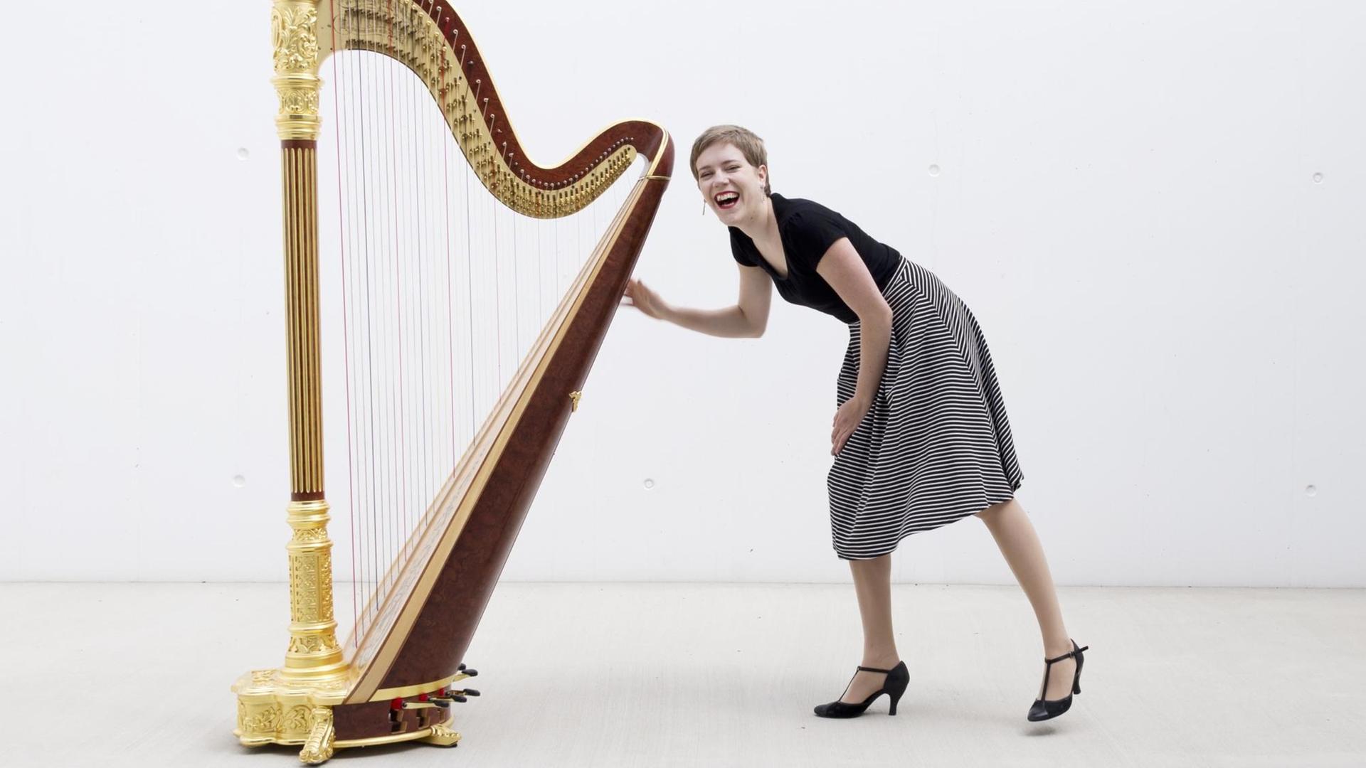 Die Musikerin Agnès Clément steht gebeugt vor ihrer Harfe und lacht in die Kamera.