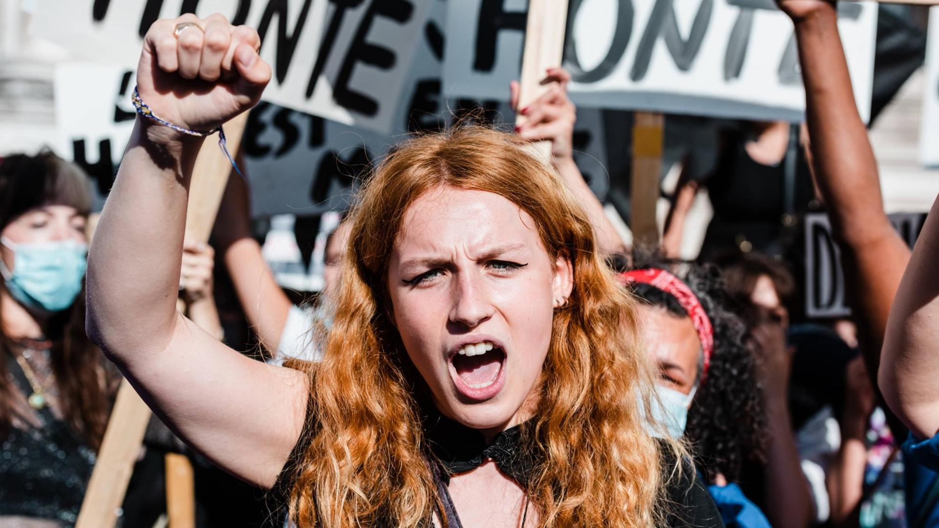 Frauendemonstration in Paris: Im Mittelpunkt des Bildes eine junge Frau mit rotblonden langen Haaren, die eine Faust in die Höhe gereckt hat. Im Hintergrund weitere in die Höhe gereckte Fäuste und Plakate. Frauendemonstration in Paris: Im Mittelpunkt des Bildes eine junge Frau mit rotblonden langen Haaren, die eine Faust in die Höhe gereckt hat. Im Hintergrund weitere in die Höhe gereckte Fäuste und Plakate.
