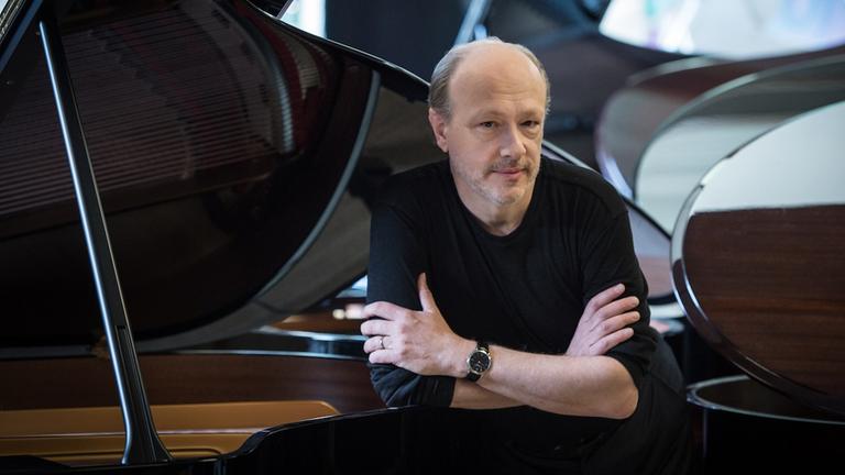 Ein Mann stützt sich in einem Raum voller Flügel auf ein Instrument und lächelt. Ein Mann stützt sich in einem Raum voller Flügel auf ein Instrument und lächelt.