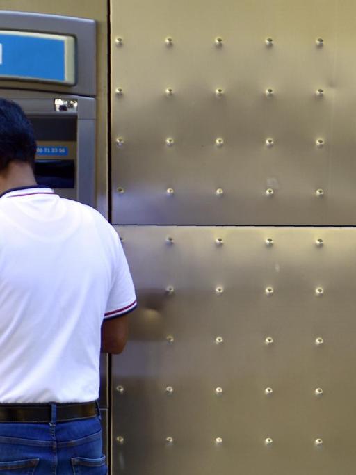 Ein Mann steht mit dem Rücken zum Betrachter vor einem Geldautomaten der Bank Sabadell.
