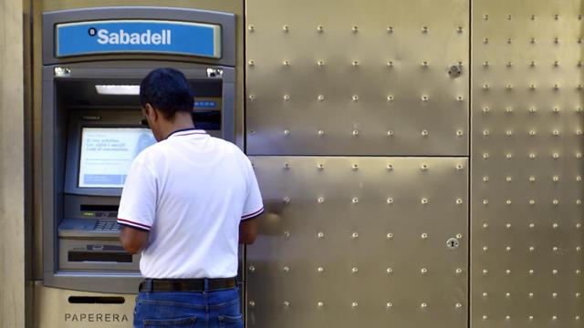 Ein Mann steht mit dem Rücken zum Betrachter vor einem Geldautomaten der Bank Sabadell.