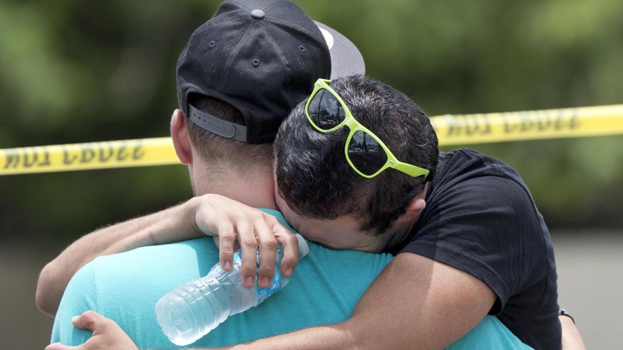 Ein Mann im blauen Shirt umarmt den anderen Mann, der zu weinen scheint.Er hat eine Brille auf dem Kopf und hält eine Wasserflasche in der Hand. Ein Mann im blauen Shirt umarmt den anderen Mann, der zu weinen scheint.Er hat eine Brille auf dem Kopf und hält eine Wasserflasche in der Hand.