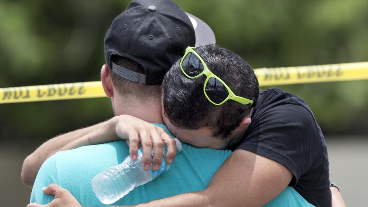 Ein Mann im blauen Shirt umarmt den anderen Mann, der zu weinen scheint.Er hat eine Brille auf dem Kopf und hält eine Wasserflasche in der Hand. Ein Mann im blauen Shirt umarmt den anderen Mann, der zu weinen scheint.Er hat eine Brille auf dem Kopf und hält eine Wasserflasche in der Hand.