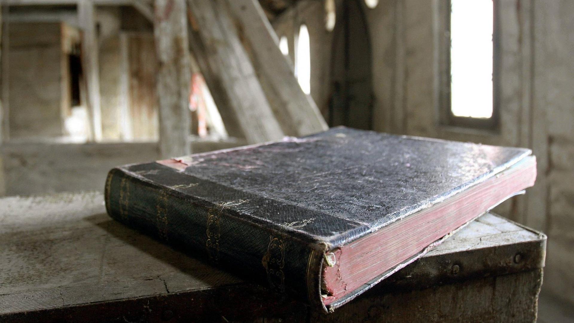 Ein historisches Buch liegt auf einer Truhe auf einem alten Dachboden.