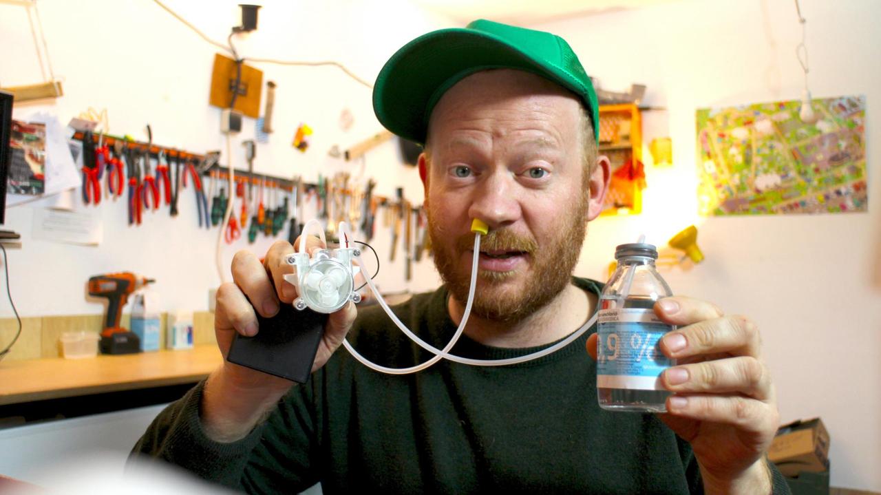 Moritz Metz in seiner Werkstatt. In der Hand hält er eine Glasampulle und eine Nasendusche. Ein Schlauch führt in die Nase. Moritz Metz in seiner Werkstatt. In der Hand hält er eine Glasampulle und eine Nasendusche. Ein Schlauch führt in die Nase.